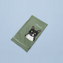 A folded green blanket with Domino’s cat portrait and name on a blue backdrop.