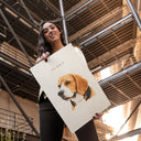 A woman holds a personalized beagle portrait poster beneath an open metal roof.