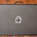A charcoal dog portrait sticker decorates a gray suitcase on a patterned rug.