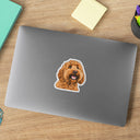 A dog portrait sticker decorates a gray laptop on a wooden desk.