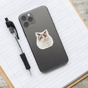 A watercolor cat portrait sticker decorates a gray phone on an open notebook.
