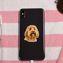A dog portrait sticker decorates a black phone on a pink striped towel.