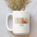 A white Milo memorial mug lies on pale fabric below dried flowers.