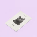 A memorial cat portrait poster lies diagonally on a lavender background.